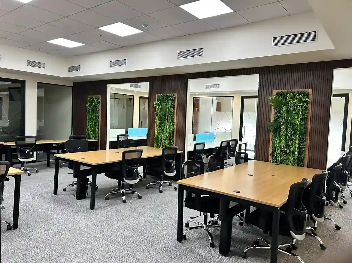 Office workspace featuring wooden group desks, black ergonomic chairs, and green vertical garden panels on a dark wood wall.