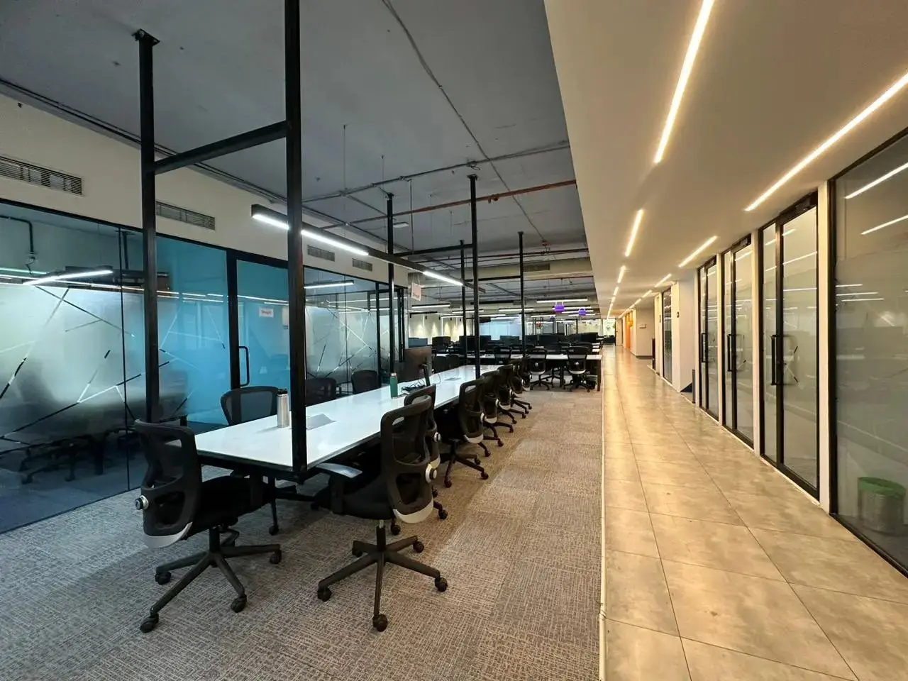 Modern office with workstations, ergonomic chairs, glass cabins, and corridor lighting
